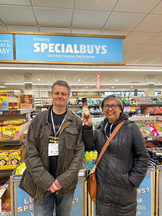 Roni and Steve in an Aldi - Roni is holding a bottle of Filipino Banana Ketchup.