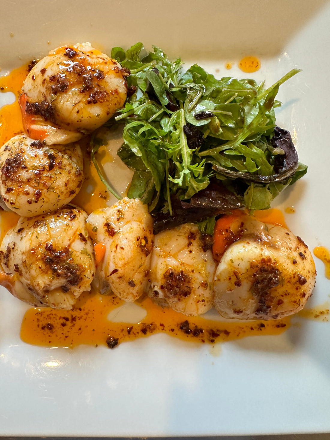a white plate with 6 large baked scallops in butter garlic chili sauce with a side salad