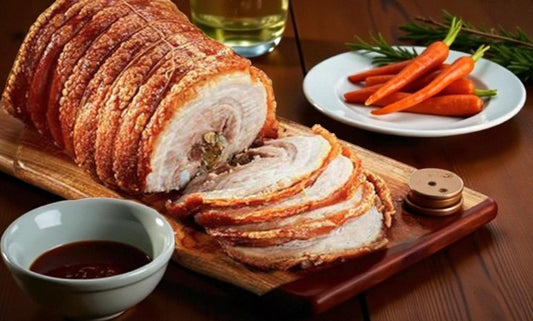 Lechon-style roast pork belly with crispy crackling, sliced and served on a wooden board with dipping sauce. Filipino-inspired festive pork dish perfect for Christmas and Noche Buena.