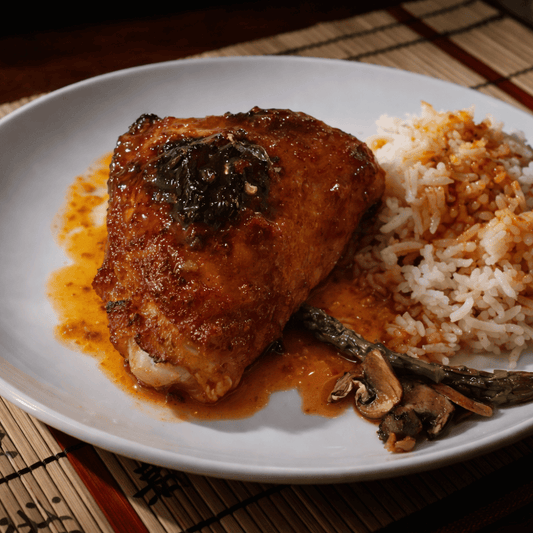 Close-up of tender chicken thighs coated in a glossy hot honey and garlic chilli glaze, served with rice and rich sauce on a white plate.
