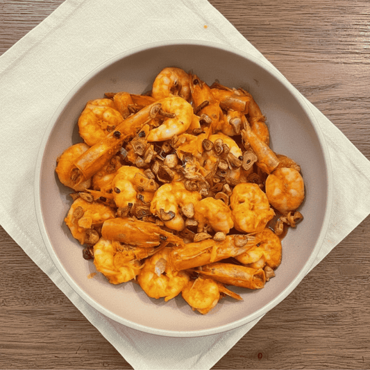 Close-up of Filipino-style gambas featuring orange prawns in a glossy garlic chilli sauce, topped with crispy toasted garlic and prawn heads, served in a neutral bowl on a wooden table.