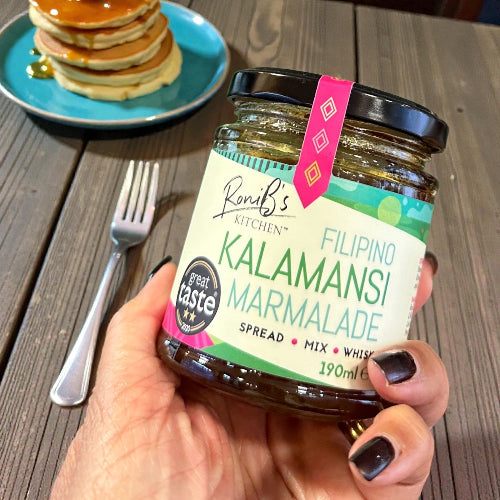 Hand holding a jar of Roni's Kitchen Filipino Kalamansi Marmalade with pancakes in the background.