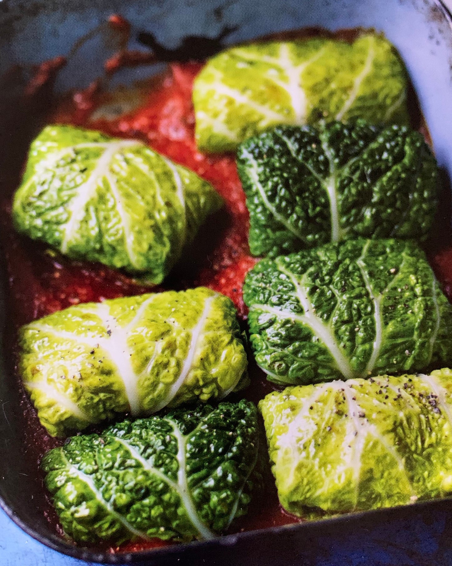 Green leafy vegetables wrapped in a red sauce in a pan
